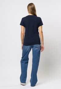 Marinblå t-shirt med korta ärmar och rund halsringning, ihop med ljusblå vida jeans. Materialet verkar mjukt och avslappnat.