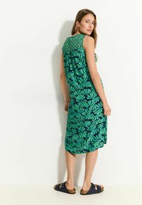 Abito floreale corto in verde e blu navy, con scollo arricciato e vestibilità ampia, caratterizzato da grandi motivi a foglia e sandali.