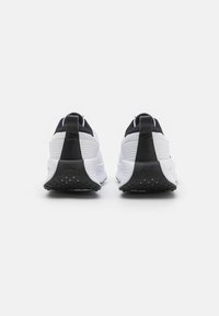 Nike running shoes featuring a white upper with black accents, textured material, and a padded heel for stability. Black rubber outsole with traction.