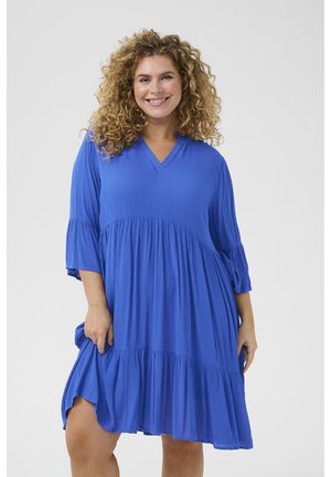 Robe décontractée bleue en tissu côtelé avec un décolleté en V, des manches trois-quarts et un ourlet évasé à volants.