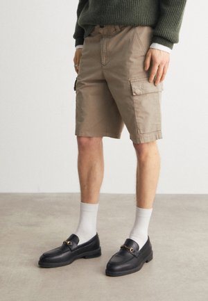 Pantaloni cargo khaki in cotone, con tasche laterali e taglio dritto. Abbinati a mocassini neri e calzini bianchi alla caviglia.