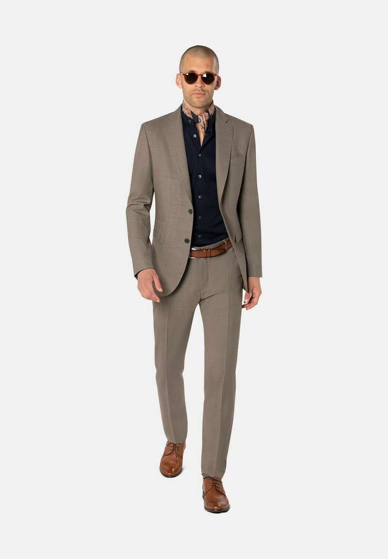 Hellbrauner maßgeschneiderter Anzug mit strukturiertem Finish, marineblaues Hemd und braune Lederschuhe, ergänzt durch runde Sonnenbrillen und einen gemusterten Schal.