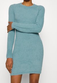 En figursydd långärmad klänning i mjukt, fuzzy himmelblått tyg med rund halsringning och ribbade manschetter, som slutar ovanför knäet.