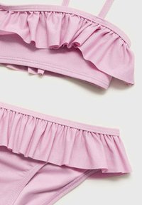 Ružový bikiny set s volánikmi pozdĺž horných a dolných okrajov. Tkanina má hladkú textúru s jemným leskom.