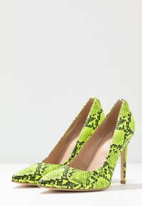Talons hauts à bout pointu en imprimé serpent jaune-vert vif. Texture lisse avec un talon aiguille et une doublure intérieure beige.