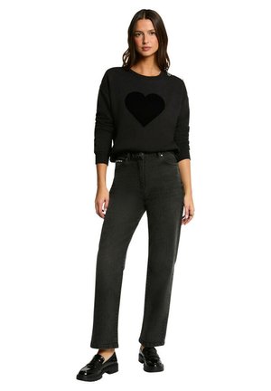 Sweatshirt noir avec un motif en forme de cœur, associé à un jean noir taille haute et coupe droite. Le mannequin porte des mocassins noirs avec une semelle épaisse.