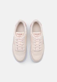 Light pink leather sneakers with white laces, perforated toe, and subtle logo accents. Smooth texture with a round toe and flat sole.