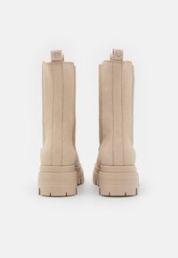 Beige ankle boots with a smooth suede finish, featuring a raised heel and vertical stitching. Designed with pull tabs for easy wear.