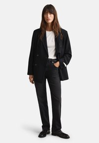 Black double-breasted blazer, white t-shirt, dark jeans, worn with black shoes. Notable details include buttons and contrasting sleeve.