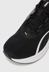 Svart idrettssko med nettingoverdel, strukturert overflate og hvite detaljer. Har snøringer og et Puma-logo på siden.