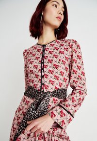 Ροζ φόρεμα με floral μοτίβο, μαύρες λεπτομέρειες, μακριές μανίκες, κλείσιμο με κουμπιά και ιμάντα με λεοπάρ σχέδιο. Λεπτομέρειες ρίγες στο στρίφωμα.