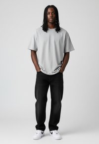 Grijs kortemouw t-shirt gecombineerd met zwarte jeans en witte sneakers. Het t-shirt heeft een ontspannen pasvorm en een zachte textuur, met een eenvoudig ontwerp.