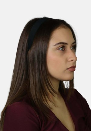 Czarna materiałowa opaska na głowę noszona przez osobę z długimi, brązowymi włosami; widok profilowy podkreślający gładki, prosty design na jednolitym tle.