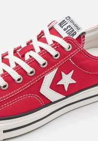 Rote Leinensneaker mit niedrigem Schnitt und weißer Gummisohle, Metallösen und Sternlogo. Verfügt über weiße Schnürsenkel und Nähte für einen Kontrast.