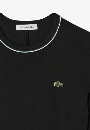 T-shirt noir avec un col rond agrémenté de bordures vertes et blanches, logo de crocodile vert brodé sur la poitrine gauche. Matériau en coton.