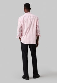 Camisa de manga larga a rayas rojas y blancas con un ajuste relajado, combinada con pantalones negros y zapatos negros. Detalles visibles en los puños de las mangas.