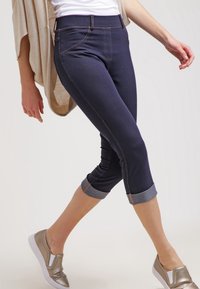 Mörkblå beskurna leggings med en slät yta, kontrastsöm och uppvikta fållar, kombinerat med metalliska slip-on-skor.