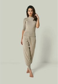 Beige geripptes Strickoberteil mit kurzen Ärmeln, kombiniert mit passenden Jogginghosen mit schmal zulaufenden Säumen und einem elastischen Bund. Glatte Textur.