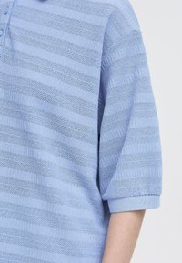 Polo shirt lavorato a maglia blu chiaro con strisce orizzontali in rilievo, maniche corte e colletto con bottoni. Tessuto morbido con polsini a costine.