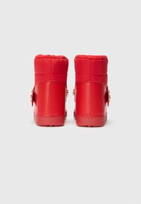 Red ankle boots featuring smooth leather, padded top, and gold hardware accents on the side. Textured outsole for grip.