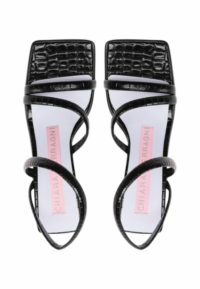 Sandali con tacco in similpelle di coccodrillo nera, con punta quadrata, caratterizzati da cinturini incrociati e un'etichetta del marchio rosa su una soletta bianca.