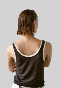 Zwarte mouwloze top met witte randen, voorzien van een rond uitgesneden achterkant en een zachte stoftextuur. Haar in een natte look gestyleerd.