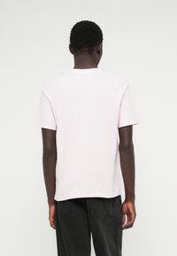 Gaiši rozā īsām piedurknēm T-krekls ar apaļu kakla izgriezumu, izgatavots no mīksta kokvilnas, ar brīvu piegriezumu un taisnu apakšmalu.