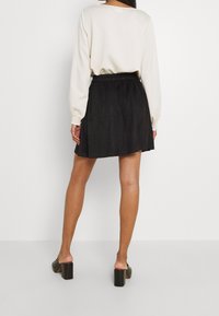 Czarna mini spódnica o gładkiej teksturze, z elastycznym paskiem w talii. W zestawie kremowy, długi rękaw. Buty na klocku.