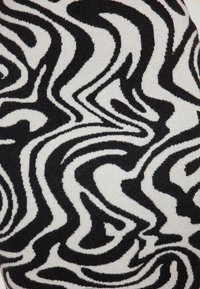 Kötött textil, amelyen egy örvénylő fekete-fehér minta látható puha szöveten, sima tapintással és kontrasztos merész vonalakkal.