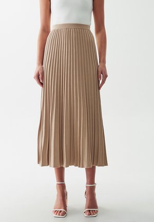 Pleated midi skirt in light beige knit fabric, featuring a high waistband and flowing design. Worn with white strappy heels.