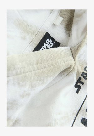 Biała tkanina o gładkiej teksturze, z czarną metką "Star Wars". Widoczne szwy wokół dekoltu oraz subtelne wariacje kolorystyczne.