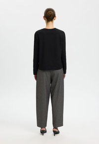 Zwarte top met lange mouwen gecombineerd met grijze wijde broek met patroon en zwarte pumps. Strak, minimalistisch ontwerp met een gladde textuur.