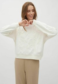 Kreemivärvi sweatshirt, mille esiküljel ja varrukatel on tekstuuriga lilleline tikand. Disainitud lõdva lõike ja soonikkoes mansettidega.