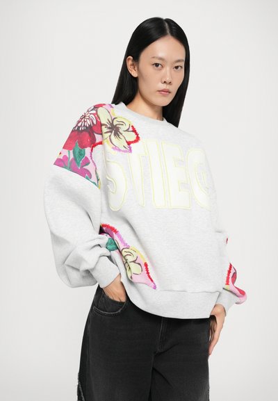 Gray sweatshirt with floral embroidery in vibrant colors on the sleeves and bold text reading "STIEG" in yellow, relaxed fit with ribbed hem.