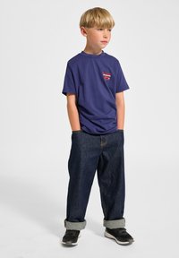 Mørkeblå bomulds t-shirt med korte ærmer og lille rødt logo, parret med opkrøllede mørkeblå denim jeans og sorte sneakers.