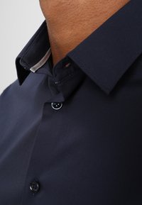 Gros plan d'une personne portant une chemise bleu marine foncé boutonnée avec un détail de col intérieur clair contrastant.