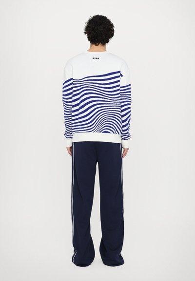 Weißer Pullover mit navy Wellenmuster, gerippten Bündchen und Saum. Kombiniert mit navy Jogginghosen mit weißen Seitenstreifen. Markenlogo auf dem Pullover.