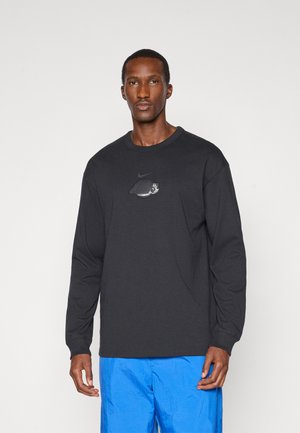 Black long-sleeve shirt featuring a small Nike logo and a circular graphic, paired with bright blue pants. Smooth cotton texture.