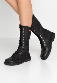 Black leather lace-up boots with silver eyelets, tall shaft, rubber sole, and side zipper. Red logo tag on the outer side. Matte finish.