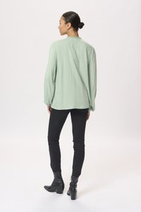 Blouse à manches longues, vert clair, avec une finition texturée et des détails froncés, associée à un jean slim noir et des bottines.
