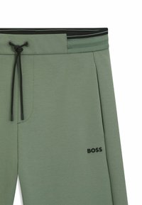 Grüne Jogginghosen mit glatter Textur, ausgestattet mit einem schwarzen elastischen Bund mit Streifen, einem Kordelzug und einem kleinen "BOSS"-Logo.