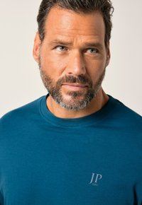Teal crew-neck t-shirt van katoen met korte mouwen, met een subtiele logo "JP 1880" op de linkerkant van de borst. Soepele textuur.