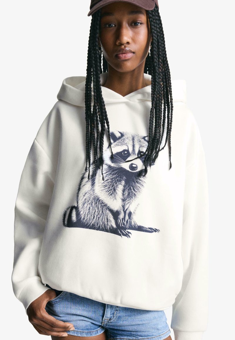 Cream hoodie featuring a raccoon graphic in navy. Made of soft fabric with a kangaroo pocket and drawstring hood. Casual fit design.