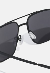 Black sunglasses with a sleek, angular design, dark lenses, and clear nose pads. Features thin metal frames and straight arms.