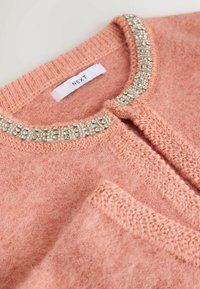 Light pink cardigan made of soft material, featuring a textured knit with a beaded neckline detail and a front closure. Label visible.