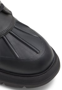 Black waterproof boot with textured rubber and smooth leather upper, featuring pleated design on the toe and a thick, rugged sole.