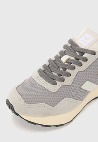 Light gray sneaker featuring mesh and suede materials, textured surface, thick cream sole, gray laces, and logo on the tongue.