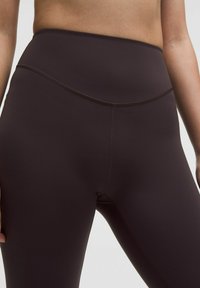 Close-up of midsection wearing high-waisted, dark brown seamless leggings with smooth, stretchy fabric and visible stitching details.