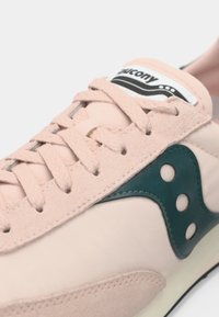 Sapatilha rosa claro com detalhes em camurça, logotipo teal na lateral com recortes circulares e etiqueta de língua branca com marca.