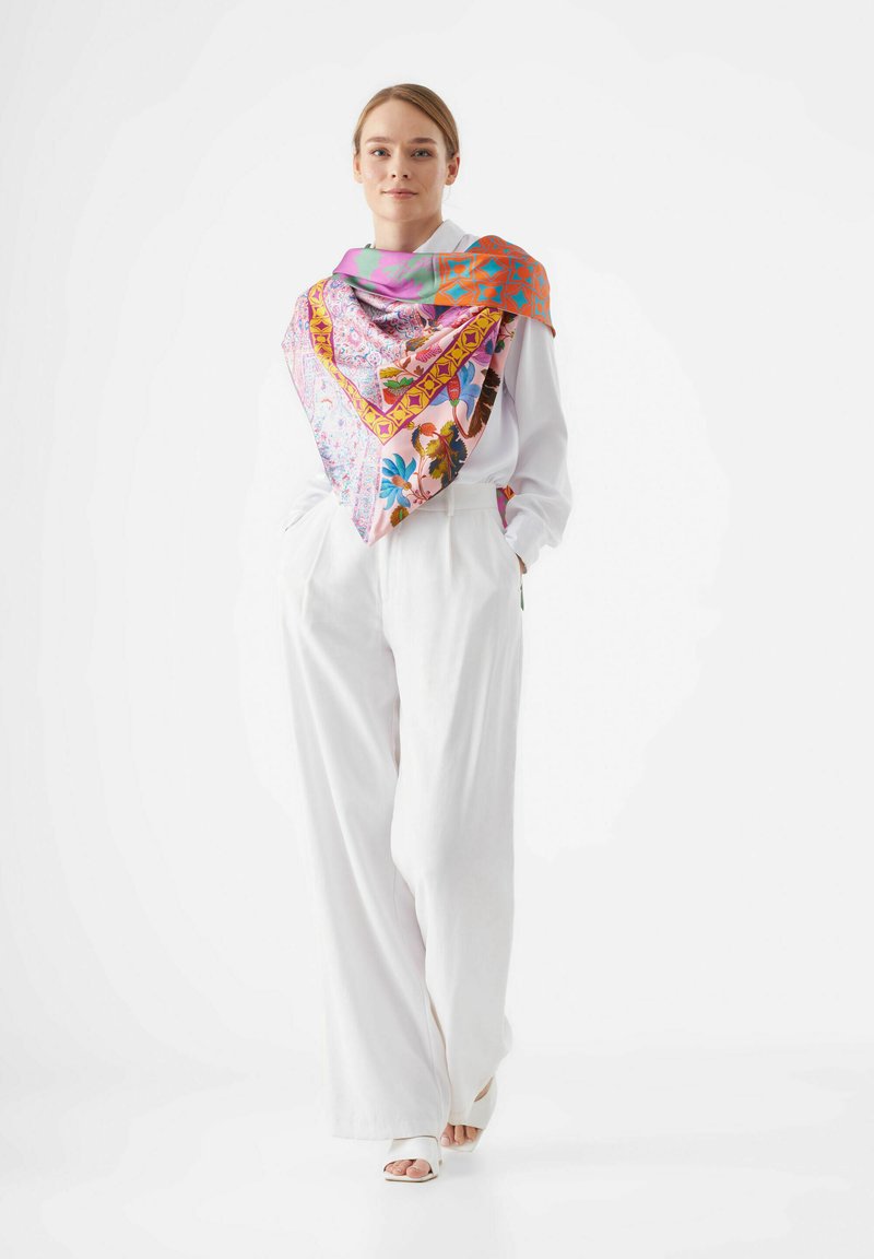 Zijden sjaal, grote vierkante vorm, levendige roze en oranje patronen, bloem- en geometrische ontwerpen, gedragen over een witte blouse en broek.